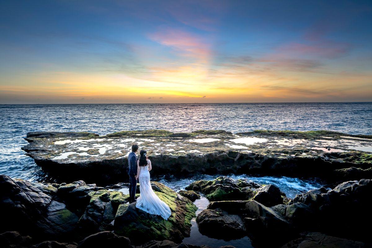 Bride and groom on a rocky shore at sunset