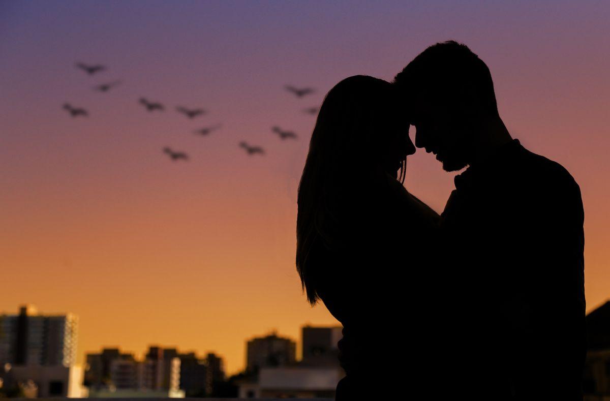 Couple in silhouette embracing under a dusk sky with birds