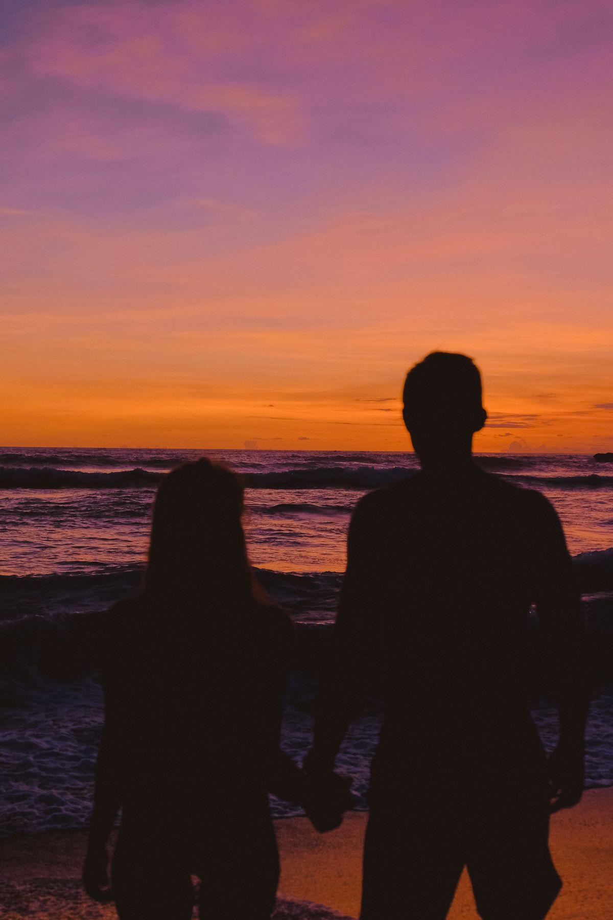 Two silhouettes facing the sea at sunset
