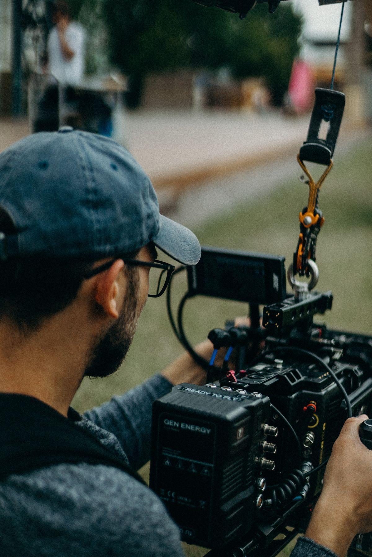 Videographer in a cap operating a cinema camera in a park