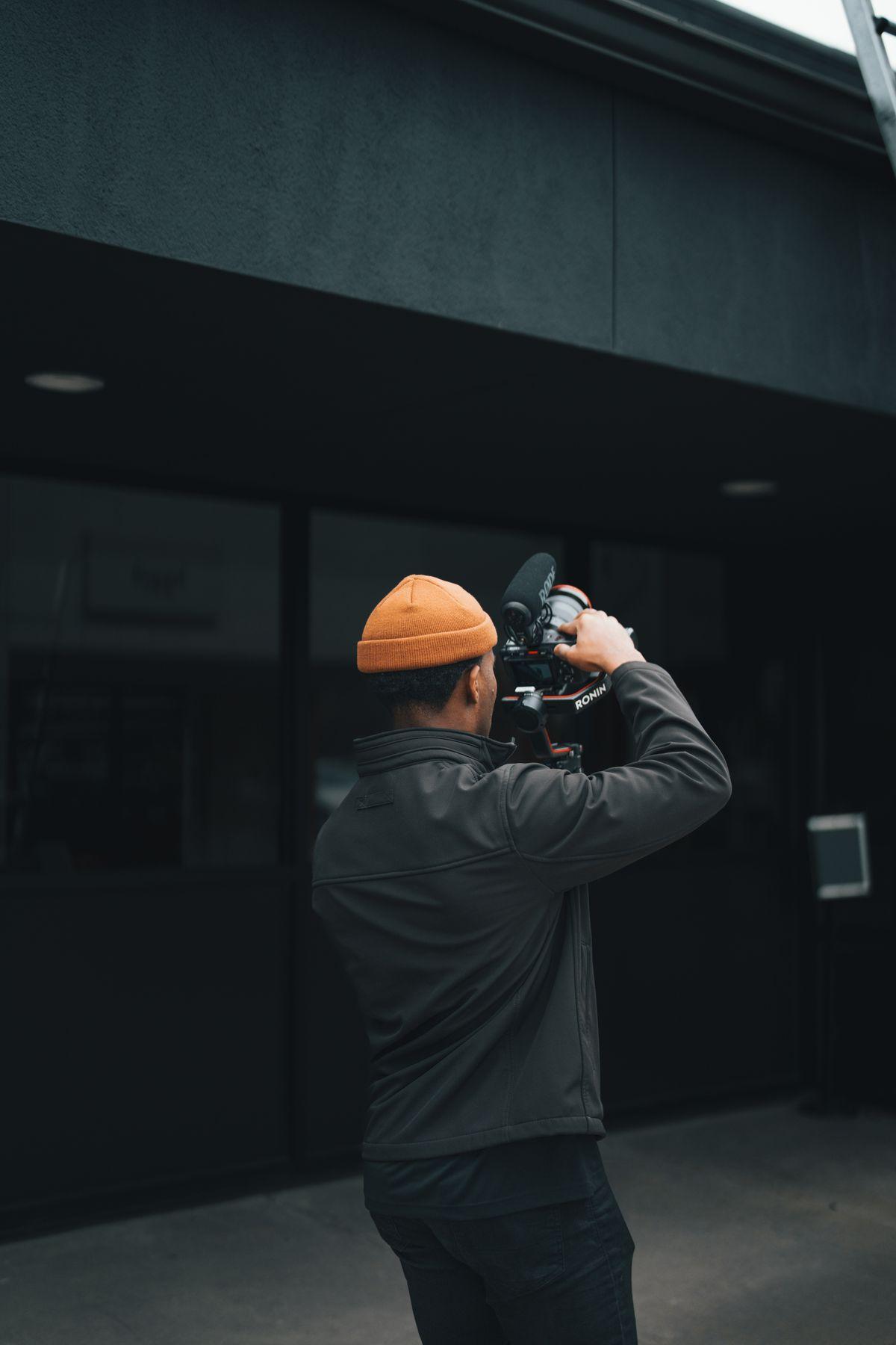 Videographer in an orange beanie filming on a street